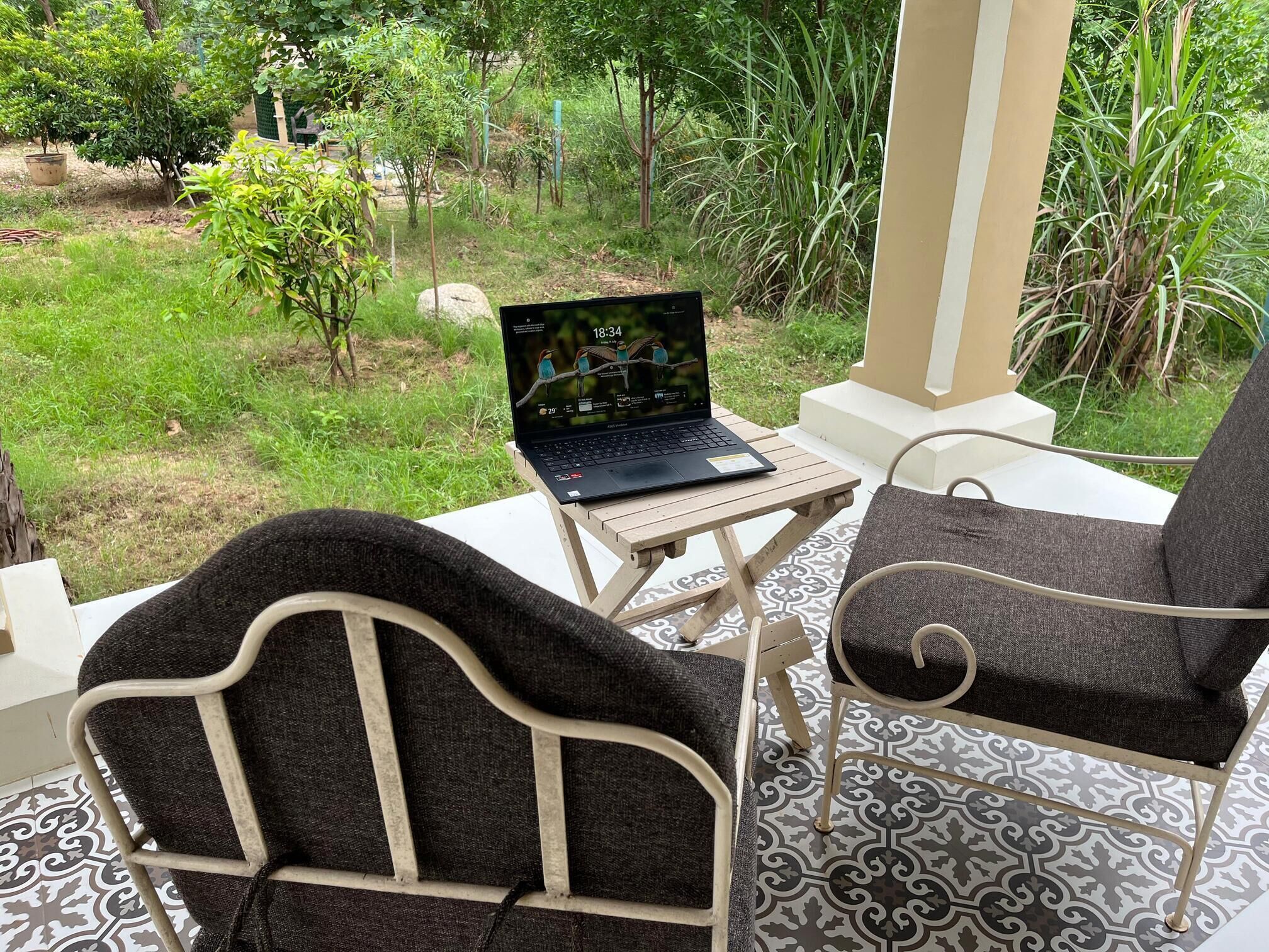 A patio with a laptop on a table, two chairs, and a view of a garden.