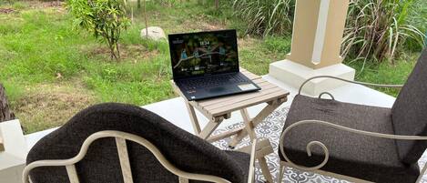 A patio with a laptop on a table, two chairs, and a view of a garden.