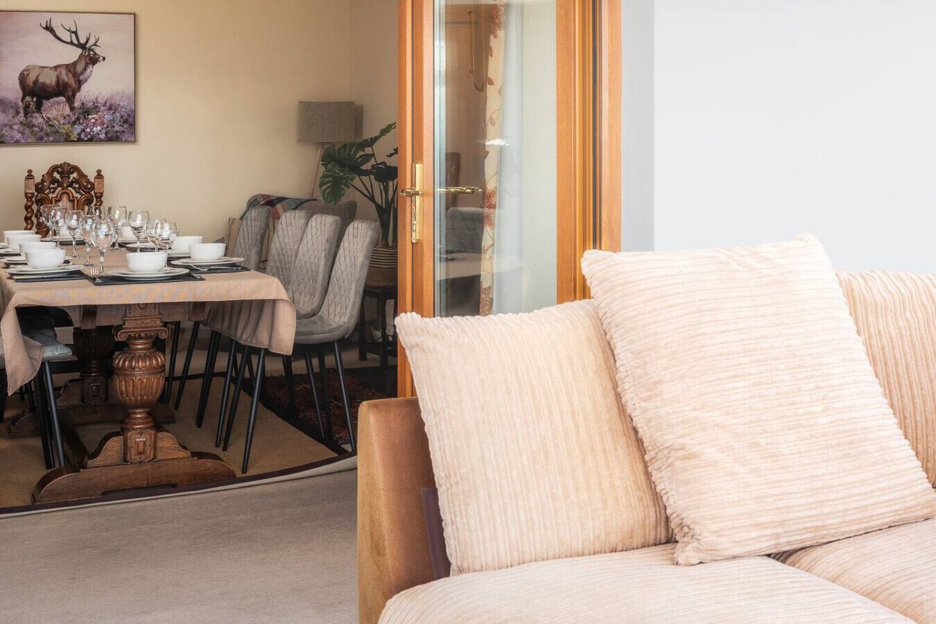 A dining area with a table set for four, a sofa with cushions, a painting of an elk, and a plant.