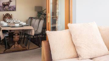 A dining area with a table set for four, a sofa with cushions, a painting of an elk, and a plant.