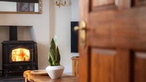Una habitación acogedora con una estufa de leña, un florero blanco con una planta y una mesa de madera.