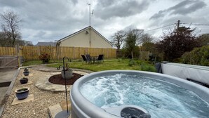 A hot tub in a backyard with a wooden fence, a house, and potted plants. - Traditional Country Cottage (Pennant)