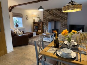 A cozy living room with a fireplace, a dining table set for two, and a comfortable sofa. - Traditional Country Cottage (Pennant)