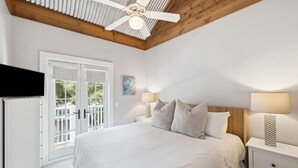 A bedroom with a large bed, a ceiling fan, a TV, and a view of the outdoors through a sliding door.