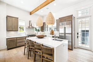 A modern kitchen with a large island, wooden cabinets, stainless steel appliances, and wicker chairs.