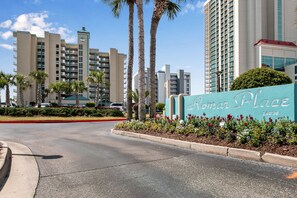 Een hotelentree met een bord waarop 'Romar Place' staat, palmbomen en moderne gebouwen op de achtergrond.