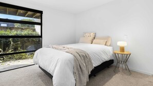 A bedroom with a large window, a bed with white bedding, a throw blanket, and a bedside table with a lamp. - All Black # 10 (Hamilton)