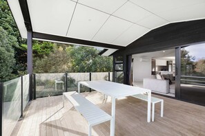 An outdoor patio with a white table and bench, surrounded by glass railings and a view of a modern interior. - All Black # 10 (Hamilton)