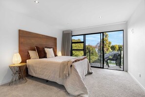 A bedroom with a large bed, a nightstand, a lamp, and a view of a balcony with outdoor furniture. - All Black # 10 (Hamilton)