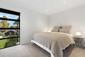 A bedroom with a large window, a bed with a beige bedspread, two bedside lamps, and a small round table with a lamp. - All Black # 10 | Luxury 5-bedroom, Sleeps 10 (Hamilton)