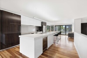 A modern kitchen with a central island, white cabinetry, and a large window providing natural light. - All Black # 10 (Hamilton)