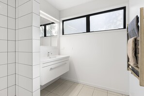 A modern bathroom with white tiles, a large mirror, a window, and a towel rack. - All Black # 10 (Hamilton)