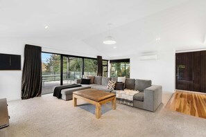 A modern living room with a grey sofa, a wooden coffee table, and a large window offering a view of greenery. - All Black # 10 | Luxury 5-bedroom, Sleeps 10 (Hamilton)