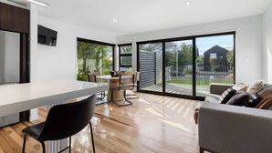 A modern kitchen with a white countertop, black chairs, and a dining table. There is a large sliding glass door leading to a patio area with a view of a house and trees. - All Black # 10 (Hamilton)