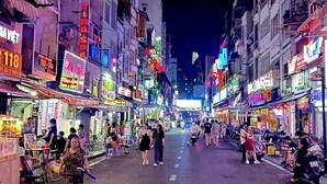 Una strada luminosa di notte, con negozi e insegne varie.