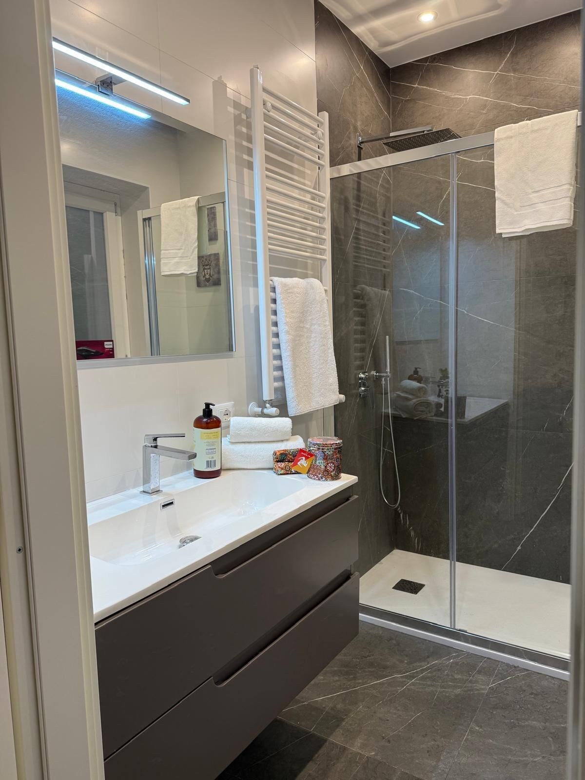 A modern bathroom with a glass shower enclosure, a white vanity with a mirror, and a dark-toned cabinet.
