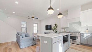A modern kitchen with white cabinets, a central island, and stainless steel appliances. There is a ceiling fan, recessed lighting, and a flat-screen TV mounted on the wall. - New River Oaks •  River Ranch • King • A+ Location • Premier Host • EV Charger (Lafayette)