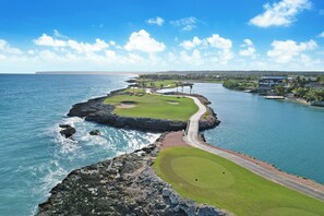A coastal golf course with a waterway, a bridge, and buildings in the background.