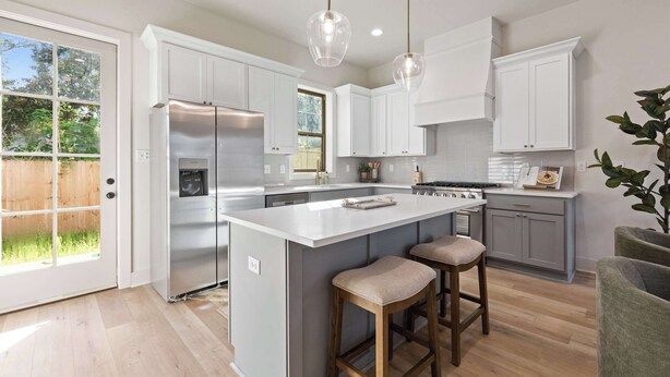 A modern kitchen with white cabinets, a central island with stools, stainless steel appliances, and pendant lighting.