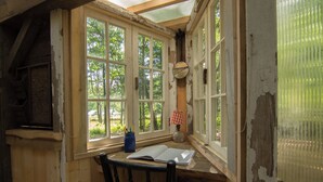 A rustic room with a wooden desk, a chair, and a large window with peeling paint. - Outlier Inn Tiny House 4 on Farm Upstate Catskills (Woodridge)