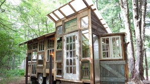 A rustic cabin with multiple windows and a wooden deck, surrounded by trees. - Outlier Inn Tiny House 4 on Farm Upstate Catskills (Woodridge)