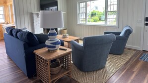A living room with a blue sofa, a patterned armchair, a wooden coffee table, and a television. -  Charming Cottage w/ WiFi, AC in York, Walking Distance to Long Sands Beach (York)