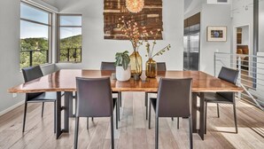 A modern dining room with a large wooden table, black chairs, and a decorative wall with a wooden panel and floral arrangement.