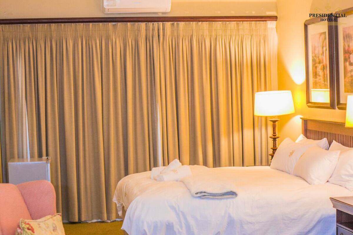 A hotel room with a bed, a desk, a chair, a lamp, and a large window with curtains.
