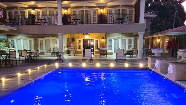 A large swimming pool with a wooden deck in front, surrounded by outdoor seating and a two-story building with balconies. - Presidential Boutique Hotel (Durban North)