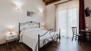 Un dormitorio con cama, lámparas de noche, escritorio, silla, televisor y ventana con cortinas.