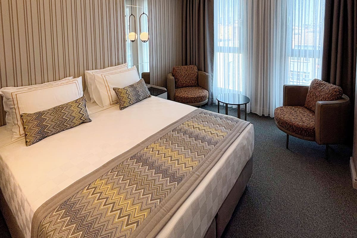 Habitación de hotel con una cama grande, dos sillones, una mesita y una lámpara en el techo.