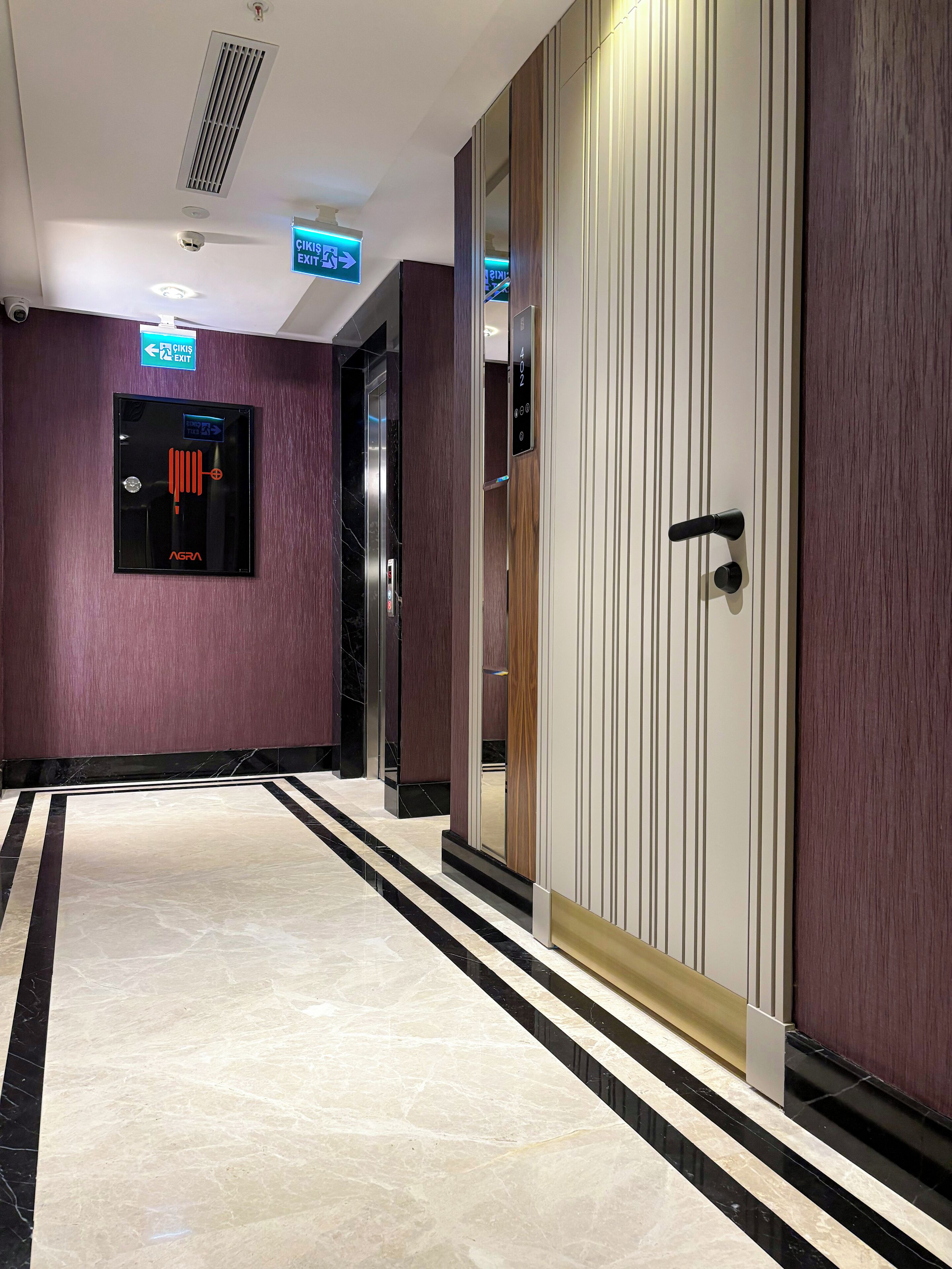 A modern hallway with a marble floor, an elevator, and a door with a digital display.