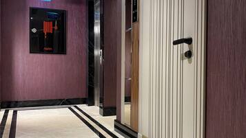 A modern hallway with a marble floor, an elevator, and a door with a digital display.