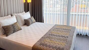 A hotel room with a large bed, a mirror, a window with curtains, and a ceiling light fixture.