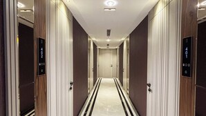 En modern hotellkorridor med ett marmorgolv, träpanel på väggarna och en centralt placerad hiss.