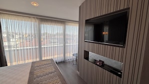 Ett modernt hotellrum med ett stort fönster, en platt-TV som är monterad på väggen, ett litet bord och en inbyggd hylla.