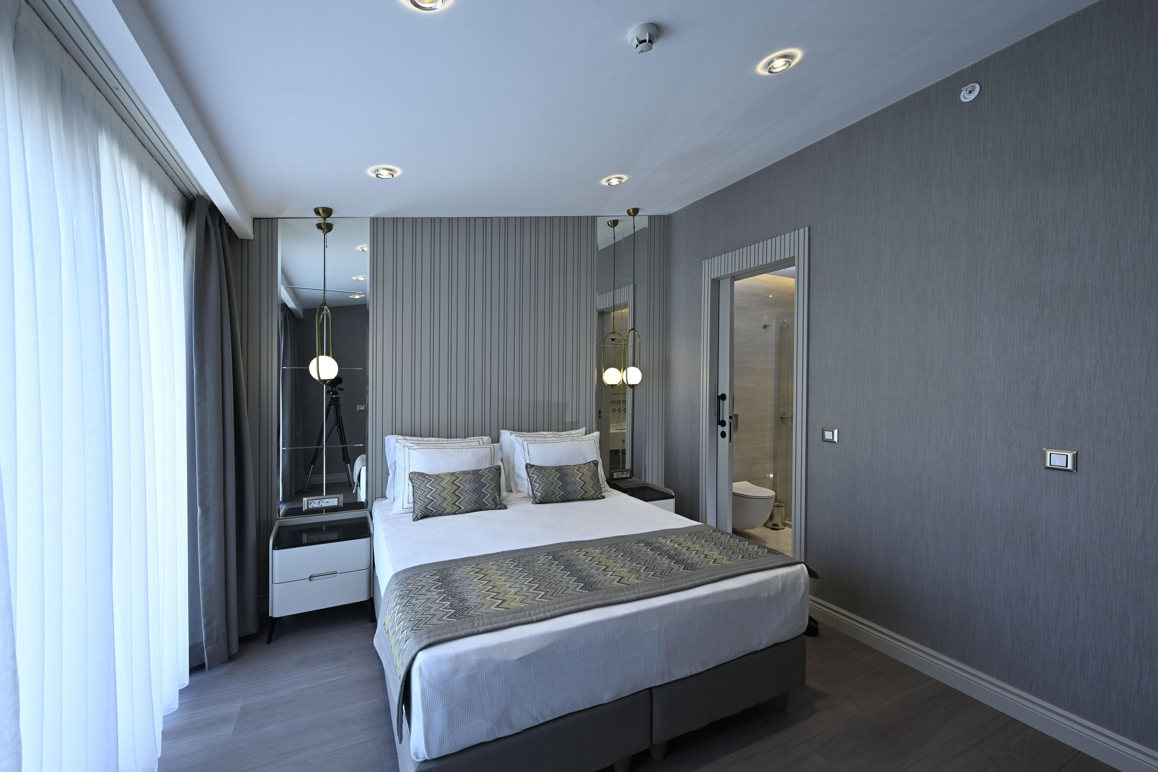 A modern bedroom with a large bed, a bedside table, a mirror, and a wardrobe.