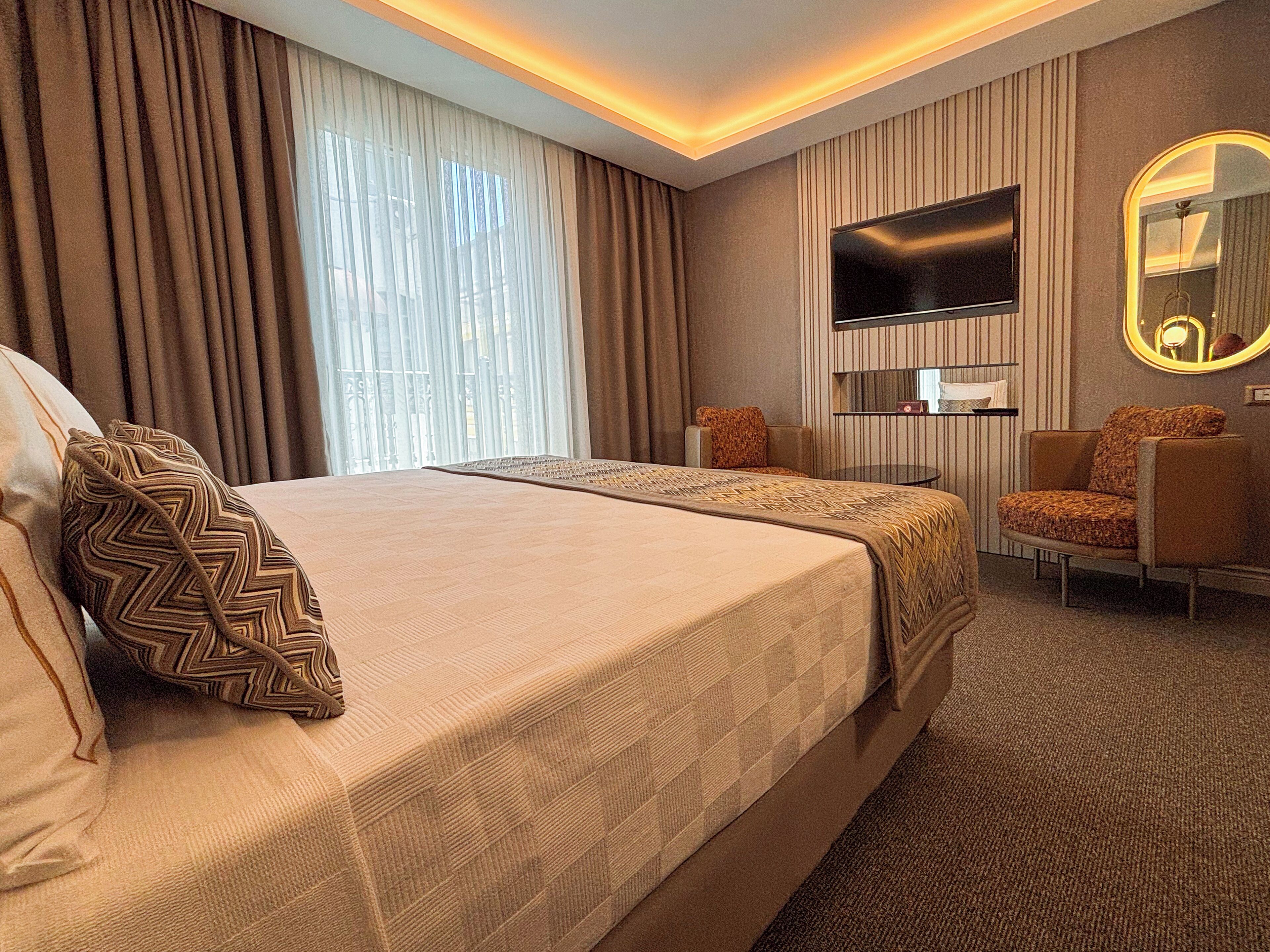 Ein Hotelzimmer mit einem großen Bett, einem Fernseher, einem Spiegel und einer Sitzecke.
