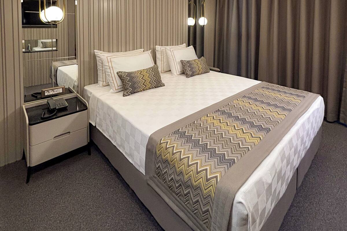 Una habitación de hotel moderna con una cama grande, mesitas de noche, un espejo y una lámpara en el techo.