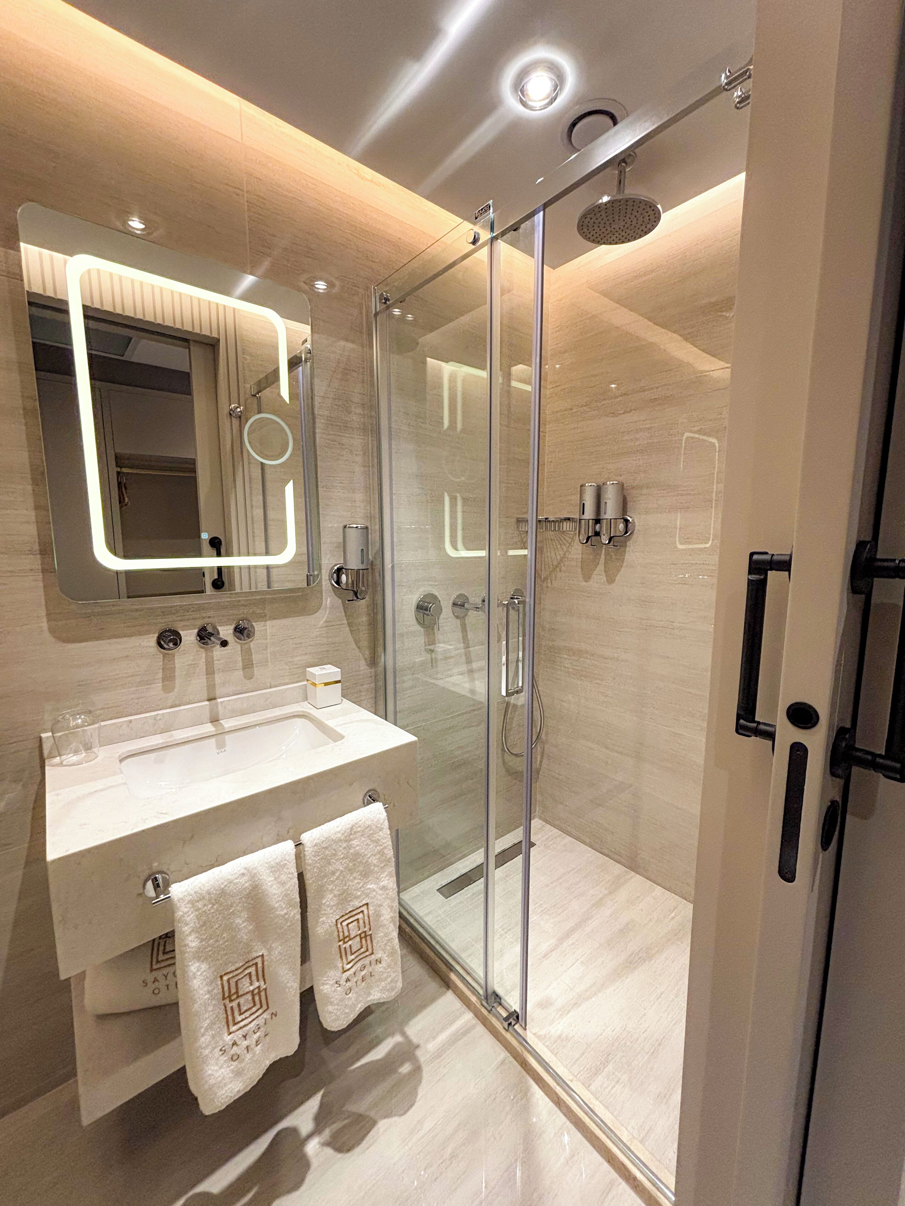 Een moderne badkamer met een douchecabine van glas, een wastafel met spiegel en twee handdoeken aan de muur.
