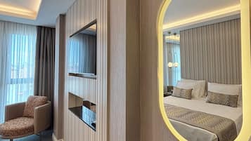 A hotel room with a bed, a TV mounted on the wall, a chair, and a large mirror with a gold frame.