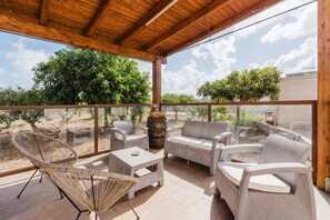 A covered patio with wicker furniture, a glass table, and a view of the surrounding greenery. - Room 'Azzarola' with Shared Garden, Wi-Fi and Air Conditioning (Rilievo)