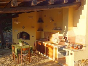Un espace cuisine extérieur accueillant, avec une table et des chaises, un luminaire suspendu et une plante en pot.