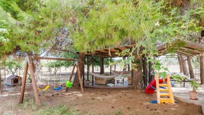 Un espace extérieur abrité comprenant un hamac, des balançoires, un toboggan et une structure de jeu en bois.