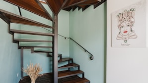 A spiral staircase with dark wood steps and metal railings, a vase of dried plants, and a framed artwork on the wall.