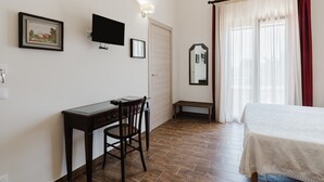 A bedroom with a bed, a desk, a chair, a television, a mirror, and a window with curtains.