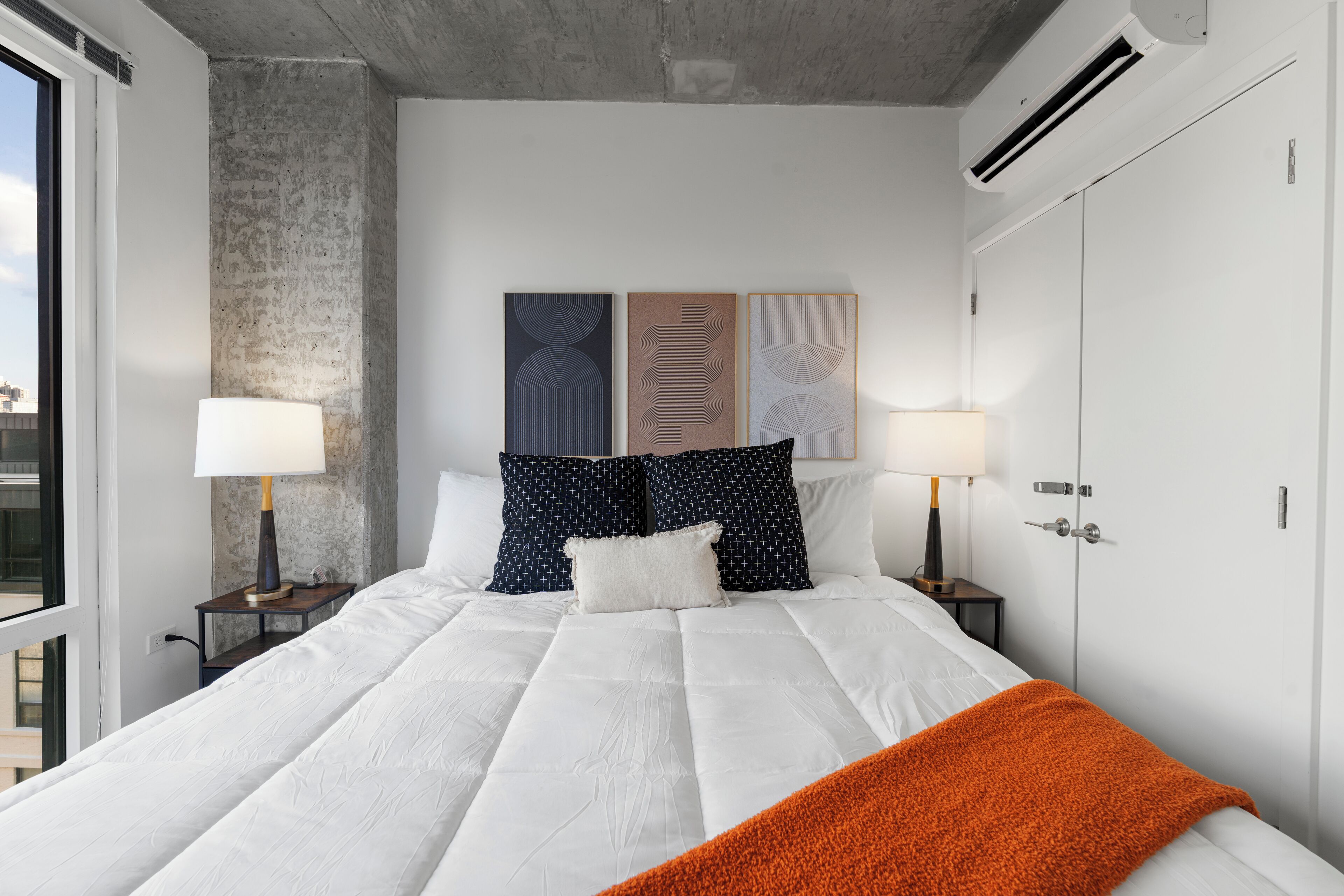 Une chambre d’hôtel avec un grand lit, deux tables de chevet avec des lampes, une armoire et des œuvres d’art accrochées au mur.