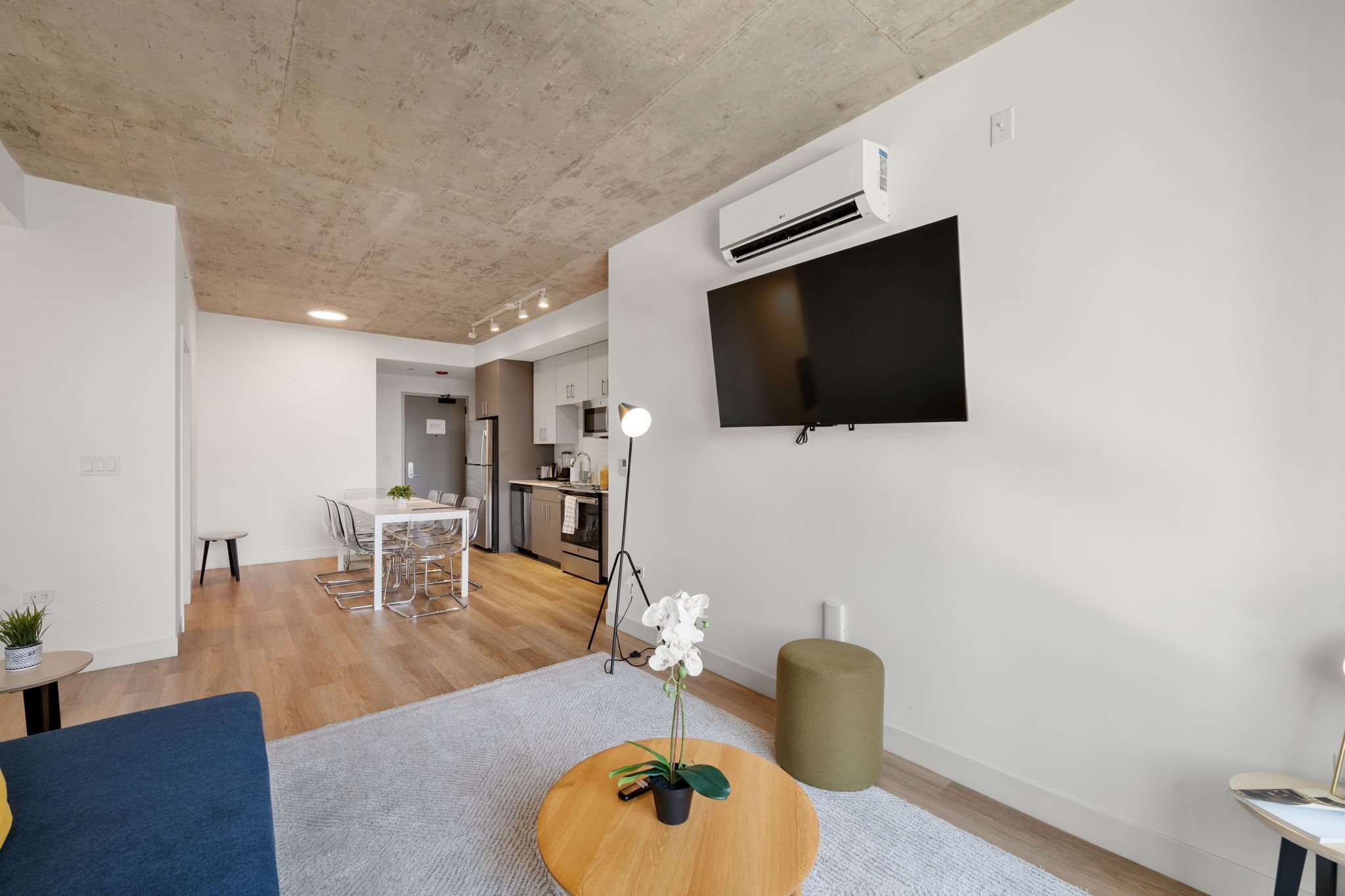 A modern living room with a flat-screen TV, a dining area, and a kitchen in the background.