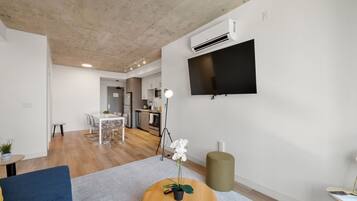 A modern living room with a flat-screen TV, a dining area, and a kitchen in the background.