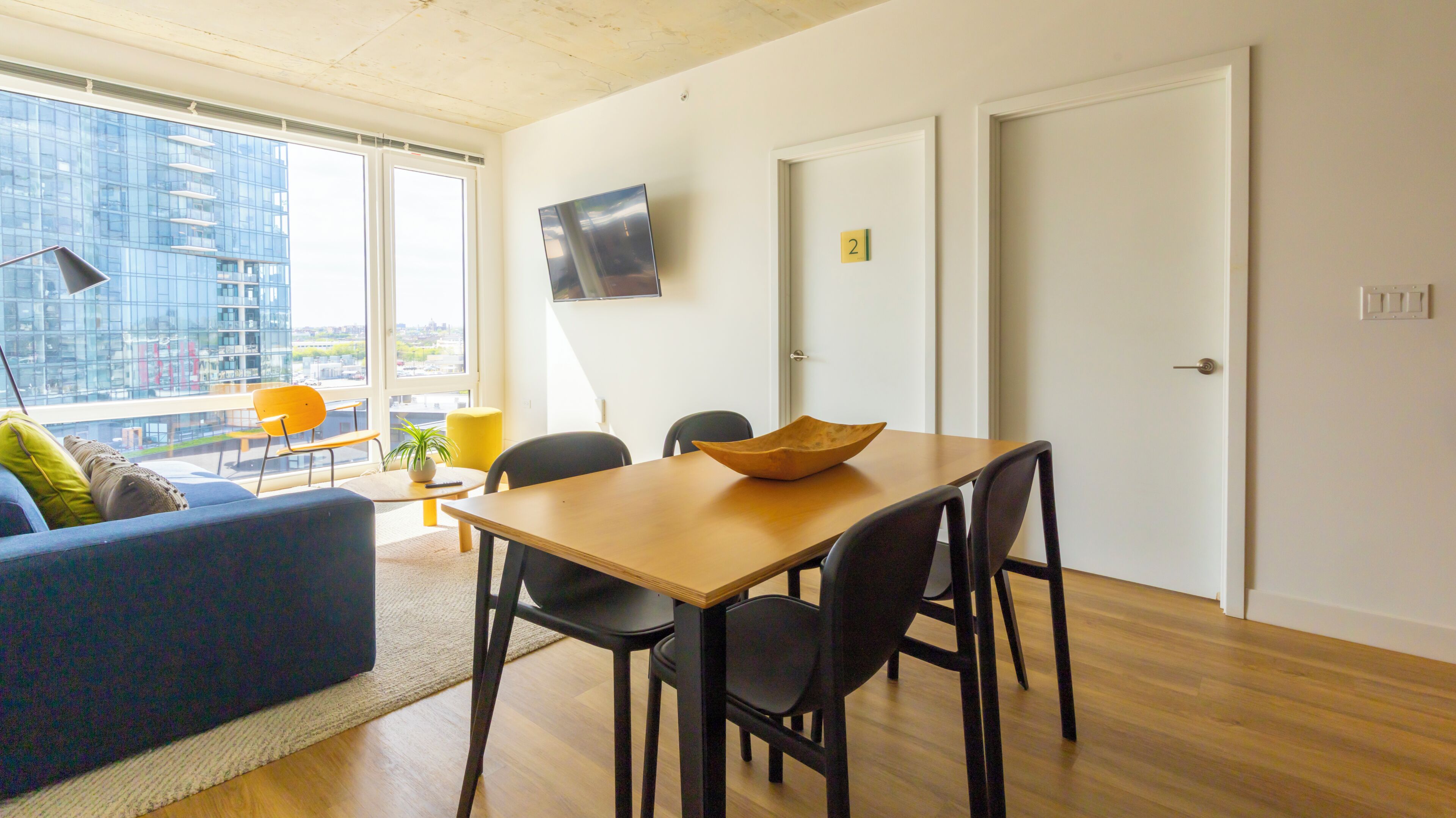 A modern living space with a dining area, a sofa, a TV, and a city view.